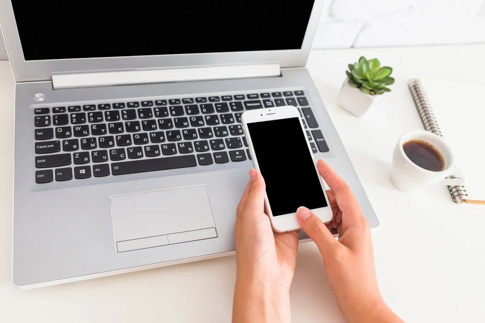 Dizüstü bilgisayarın üzerinde akıllı telefon tutan el