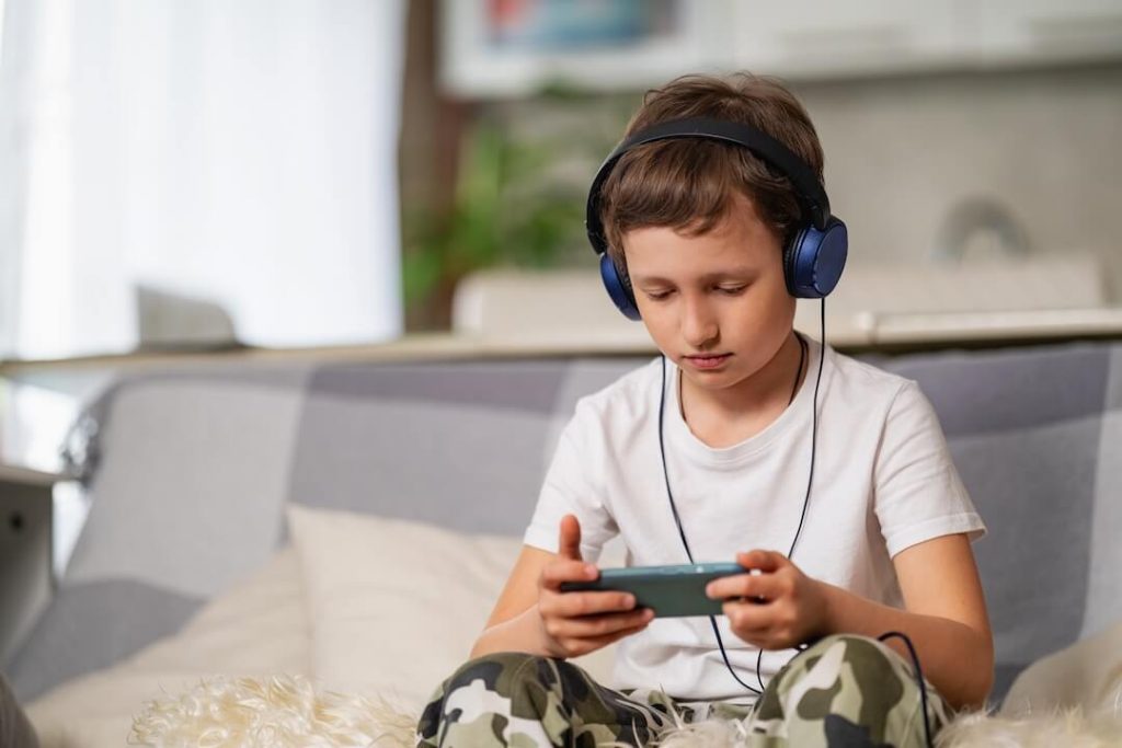 Gamer-boy-with-headphones-smartphone-his-hands-is-sitting-sofa-playing-1024x683